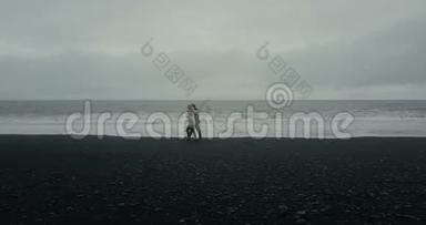 年轻夫妇在黑色火山海滩散步的鸟瞰图。 男人和女人在冰岛的海边有个约会。